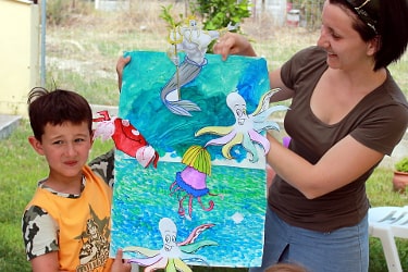 Творческий мастер-класс: ребенок и психолог рассматривают яркий рисунок с морской тематикой на занятии по арт-терапии в Греции